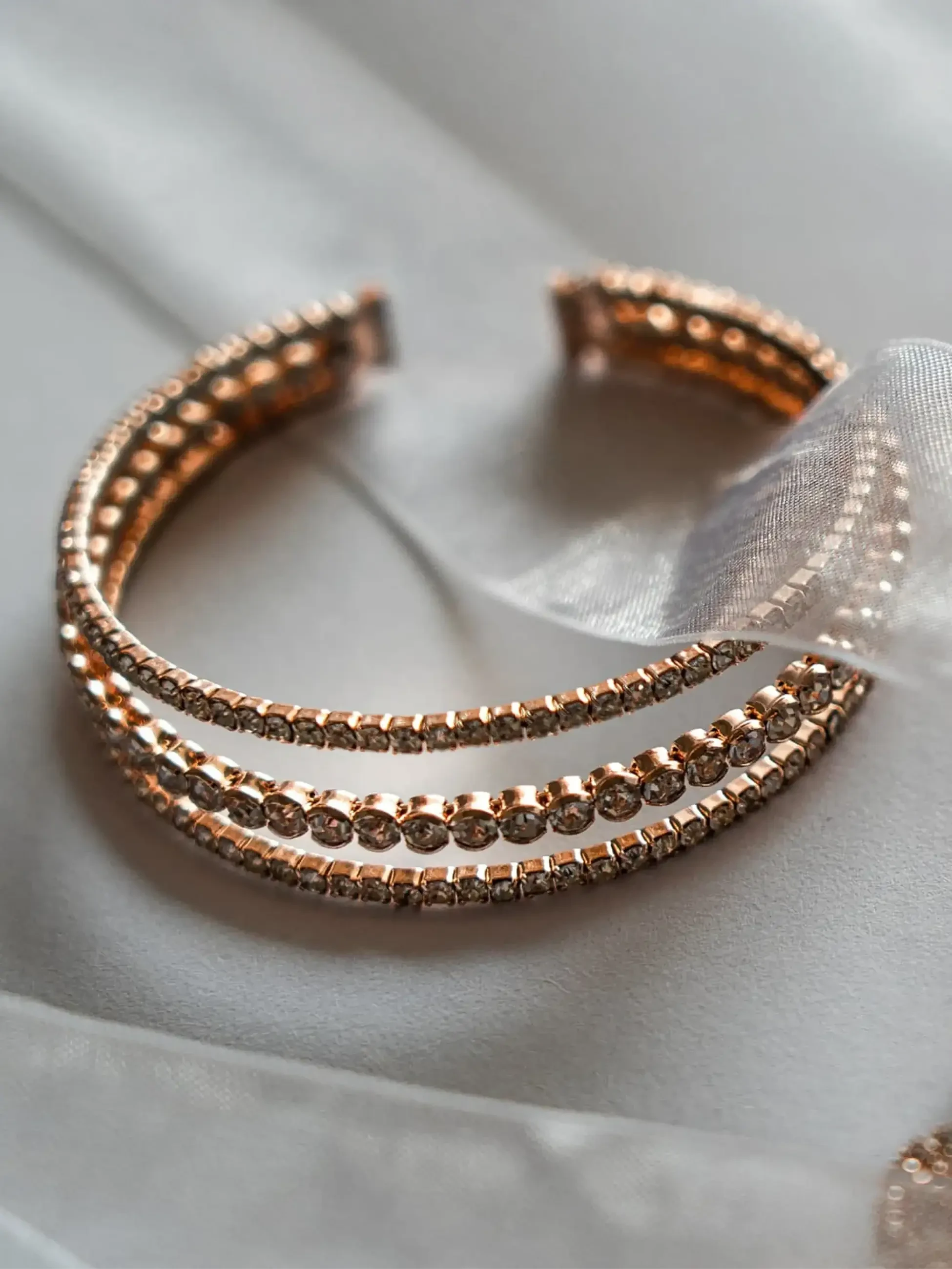 Rose gold crystal bracelet displayed on white satin with sheer ribbon.