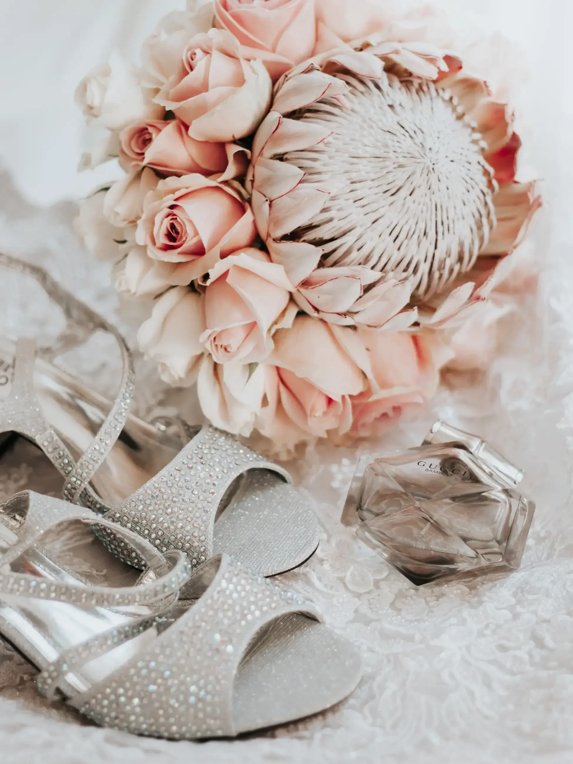 Bridal shoes, blush bouquet, and Gucci Bamboo perfume arranged on lace.
